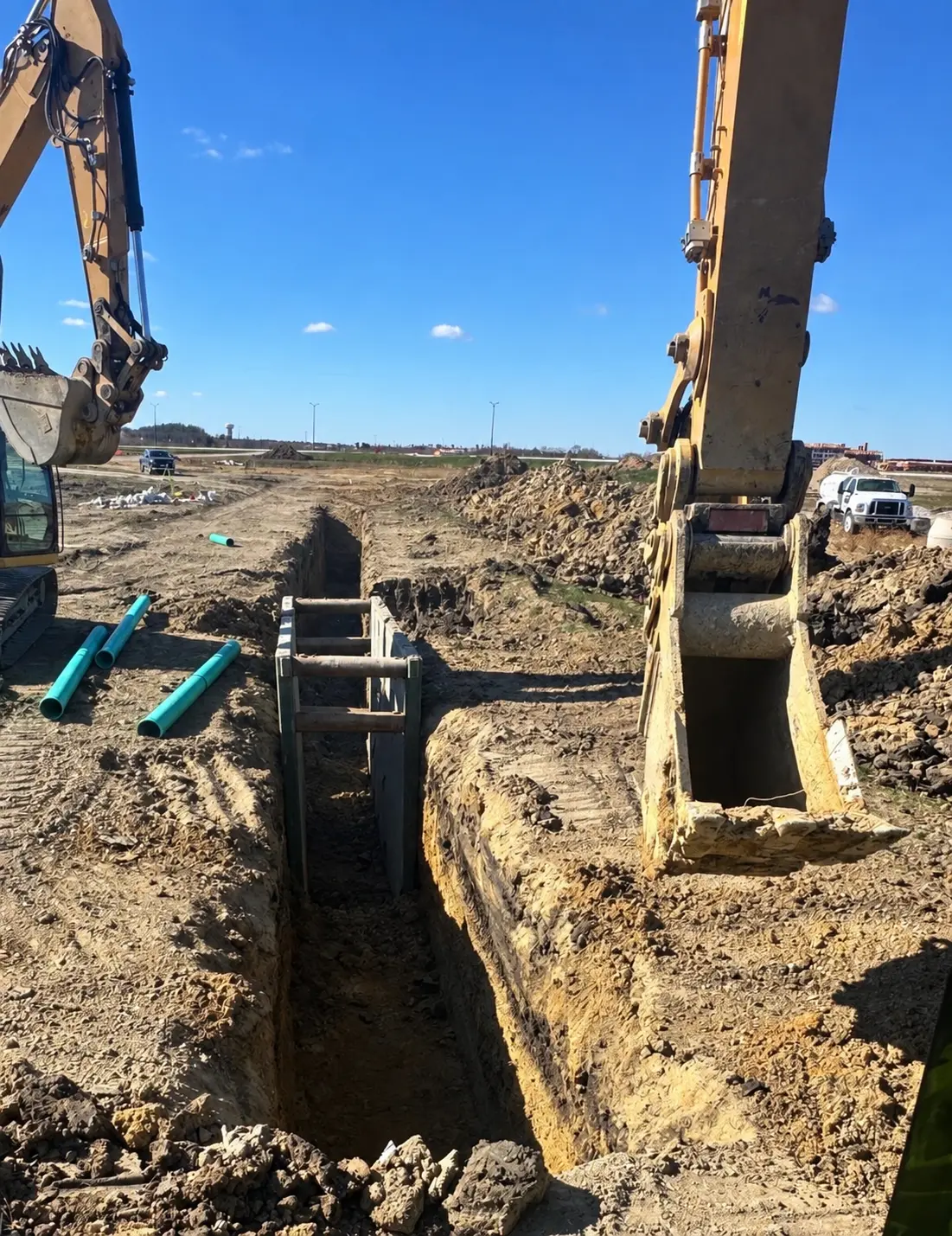 Excavator boom over an open utility trench with a trench box and PVC pipe