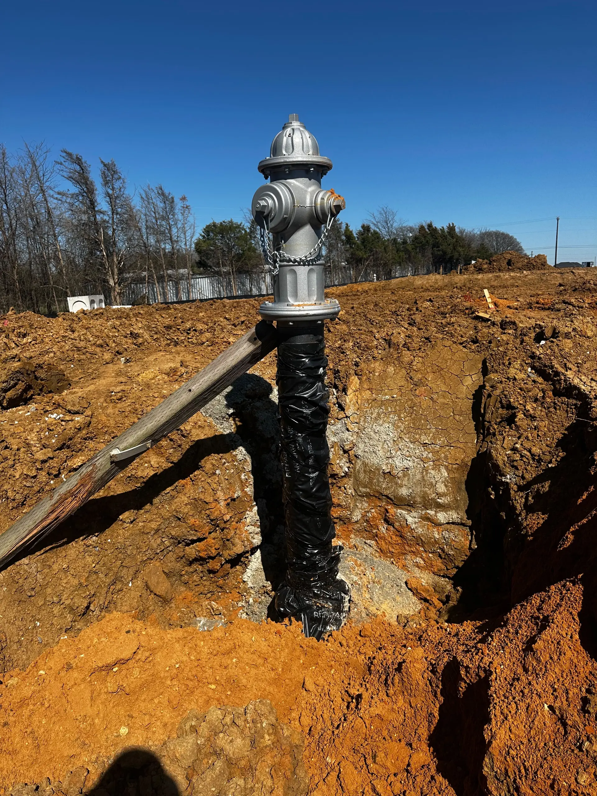 Fire hydrant and wrapped riser pipe being installed and braced in an excavation