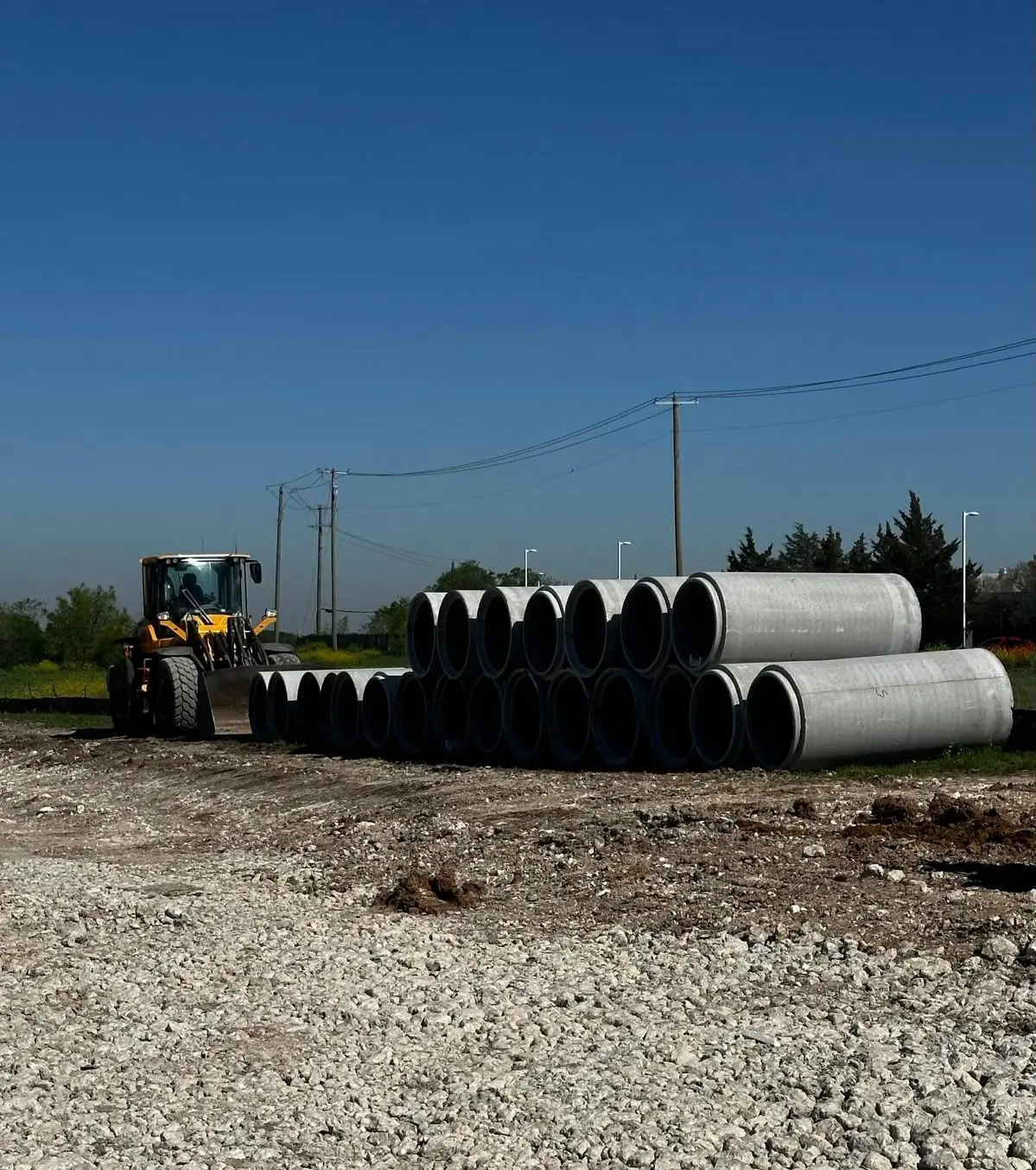 Stacked large-diameter concrete storm pipe staged on crushed rock beside a wheel loader