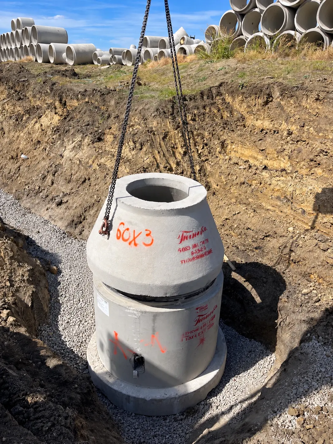 Precast concrete manhole cone marked 60X3 being set by chain hoist in an excavated hole